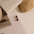 Rectangle Black Onyx Studs featuring gold and rectangular black stones rest on a white surface beside a box, a stone, and printed text, adding a timeless vintage touch.