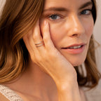 A woman with light brown hair touches her face, wearing the Everly Thin Duo Band ring with an adjustable band and a beige knitted top.