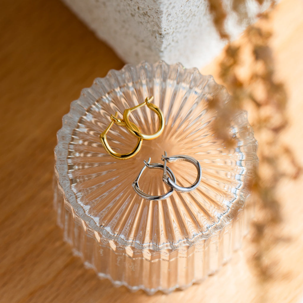 The McKenna Abstract Hoops set includes two pairs of everyday earrings—one gold and one silver—with organic-shaped hoops, beautifully presented on a clear ribbed glass container.