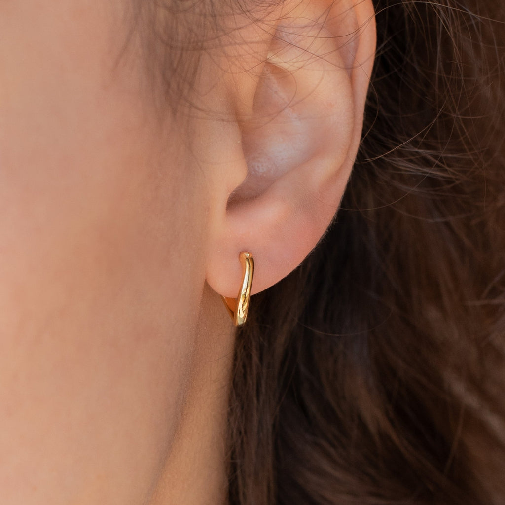 Close-up of a person's ear wearing the McKenna Abstract Hoops—small, twisted gold earrings with an organic shape, perfect for understated everyday style.