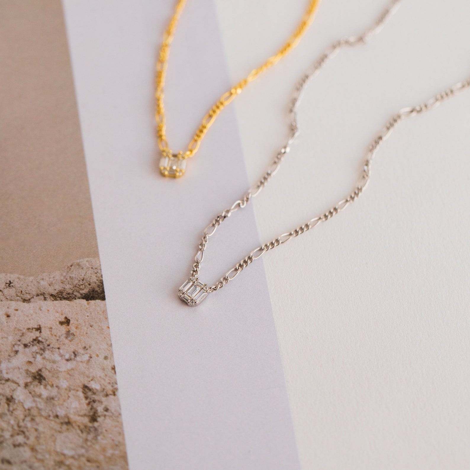 Square Diamond Figaro Necklaces, crafted in gold and silver with small square pendants—some set with sparkling baguette diamonds—are displayed on a neutral background.