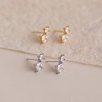 The Aria Diamond Drop Studs set includes two pairs of lightweight stud earrings—one gold, one silver—each featuring two square-cut clear stones. Perfect for any occasion, they’re beautifully displayed on a neutral background.