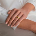 A hand with nude nails wearing the Olive Peridot Signet Ring rests gently on another person's arm in soft lighting.