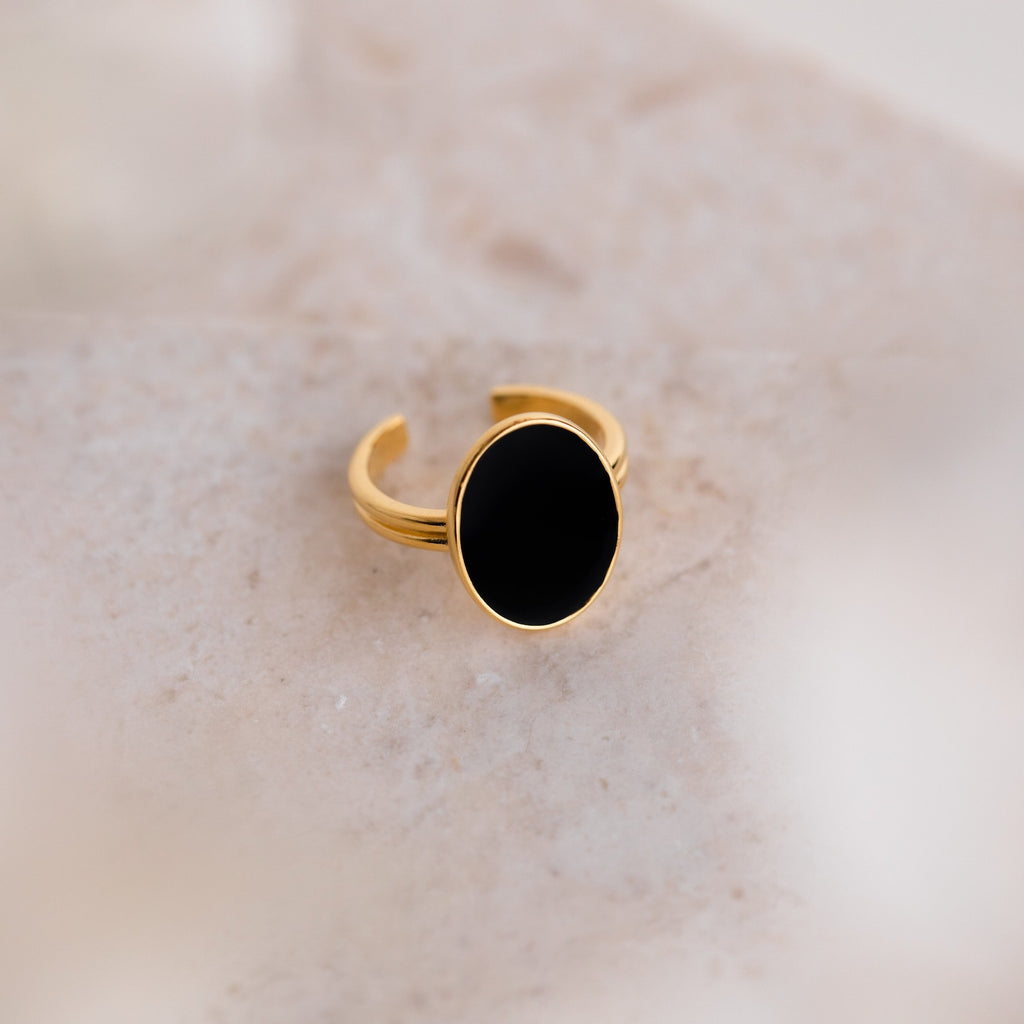 The Midnight Hour Onyx Ring features a large, oval-shaped black onyx stone and an adjustable band, showcased on a light, textured surface.