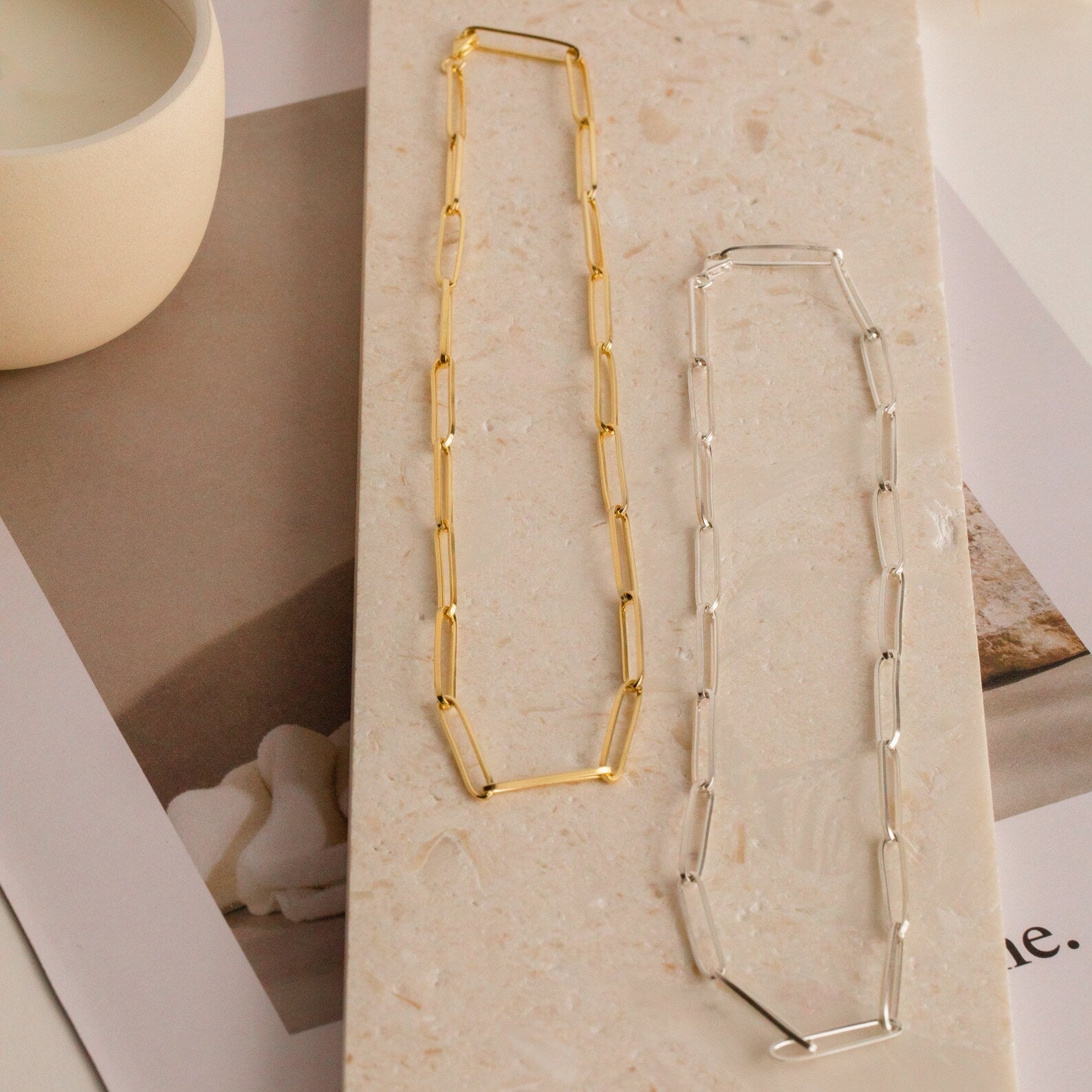 The Custom Link Chain Necklace is displayed on a rectangular beige stone slab, featuring both gold and silver options with large links.