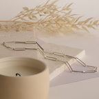 The Custom Link Chain Necklace is displayed on stone tiles next to a beige candle and dried leaves, creating a bold statement.