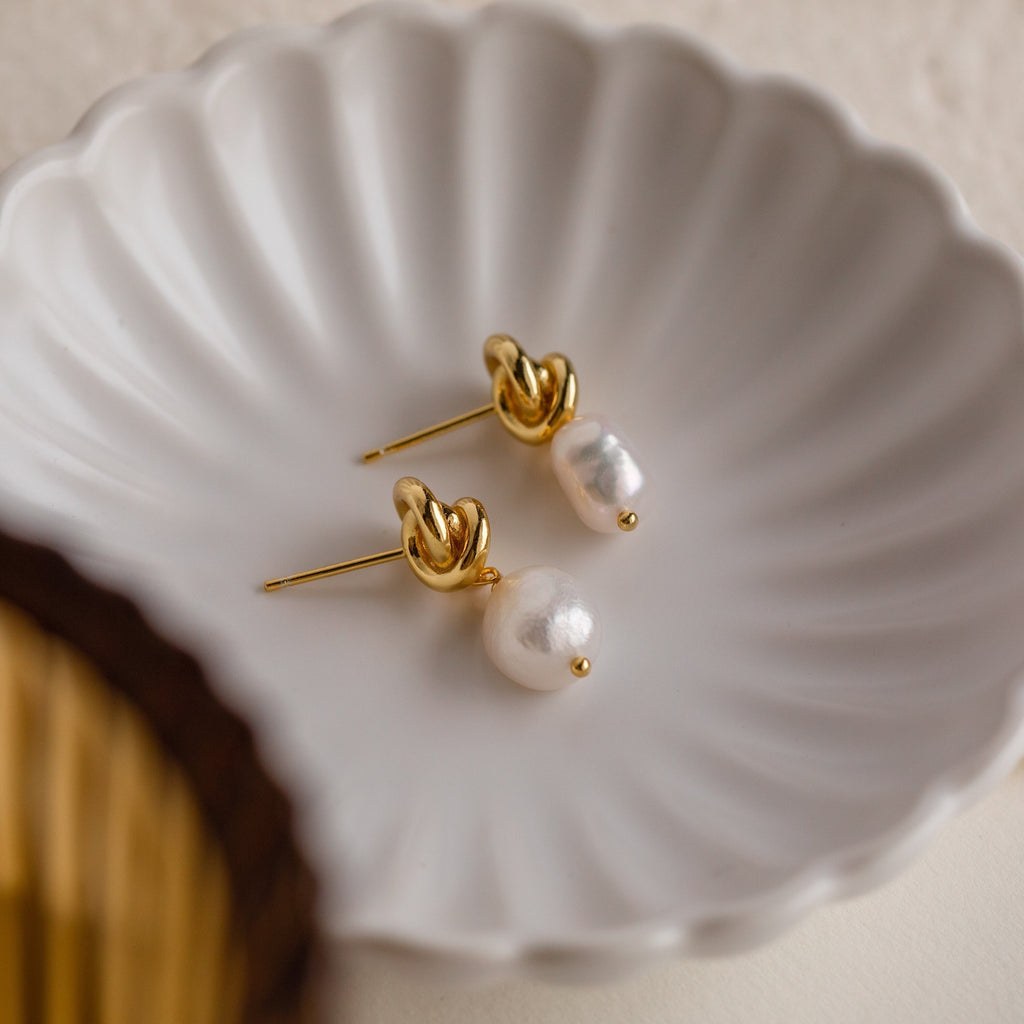 Knot Pearl Drop Earrings in 18K Gold featuring dangling pearls and a Celtic knot design, displayed on a white scalloped dish—perfect for fans of elegant, minimalist style.
