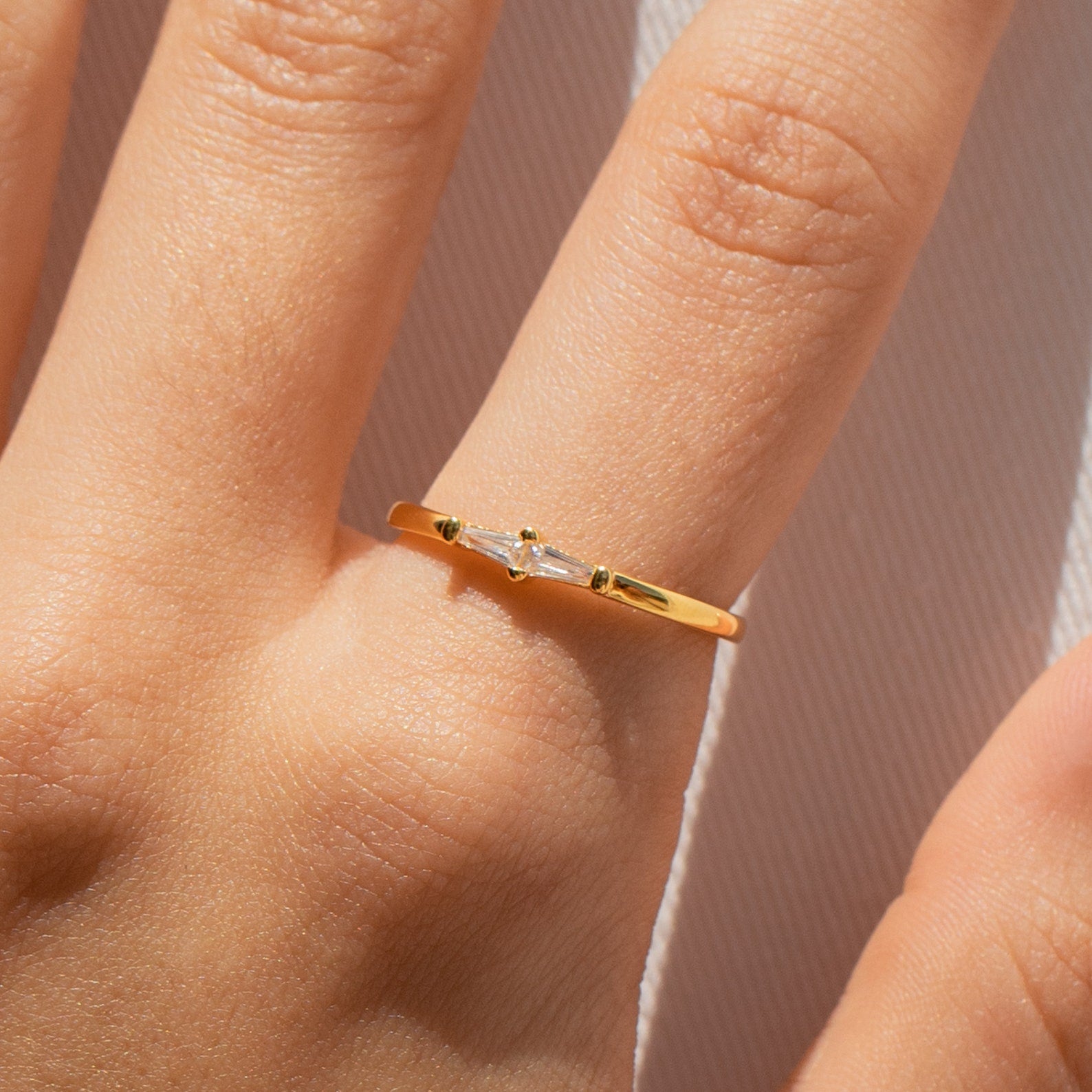 A hand wears the Eleanor Baguette Diamond Ring, featuring a thin gold band with a delicate baguette-cut diamond on the ring finger.