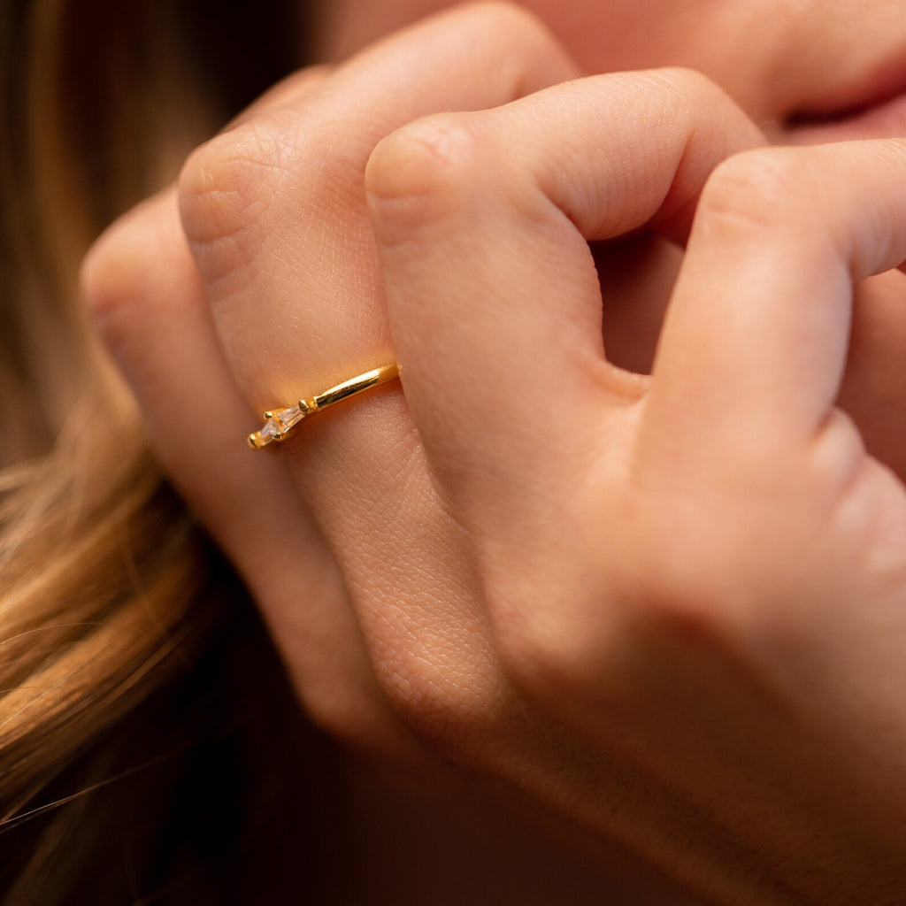 A close-up of a hand wearing the Eleanor Baguette Diamond Ring, which features a slim gold band and a small baguette diamond on the ring finger.