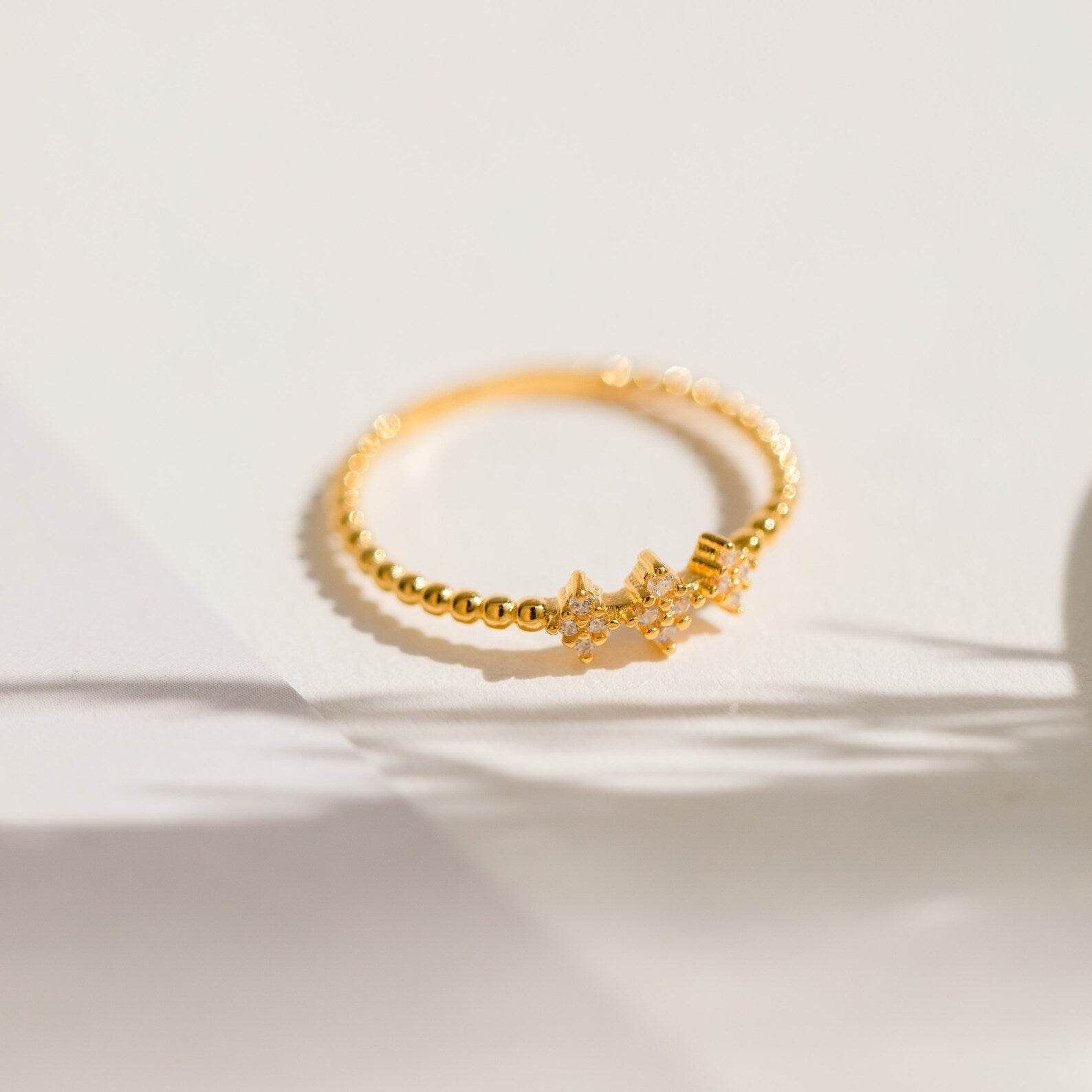 The Jasmine Beaded Diamond Ring features a gold band with a delicate star-shaped diamond cluster, perfect for stacking. Shown in soft sunlight on a white surface.