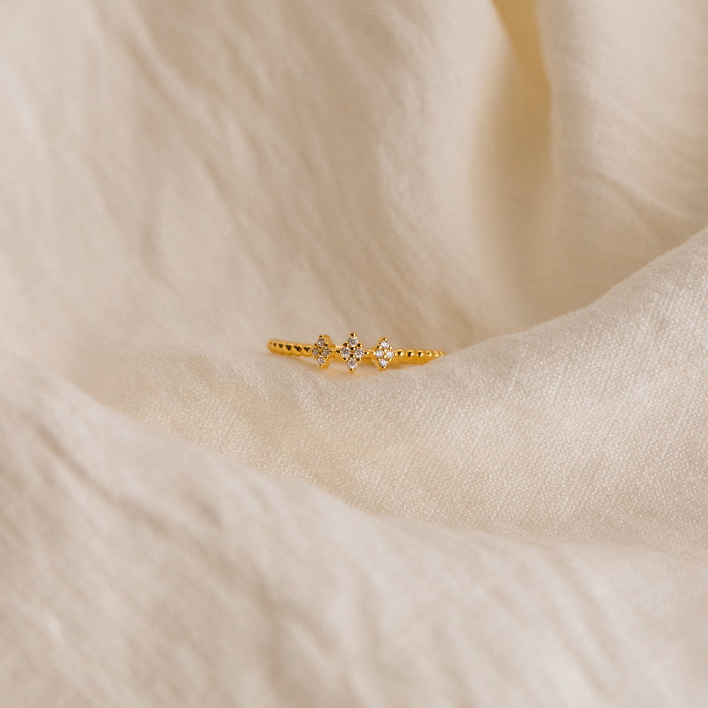 The Jasmine Beaded Diamond Ring, featuring three small diamonds, is displayed on soft cream fabric—ideal for bringing a timeless touch to your ring stack.