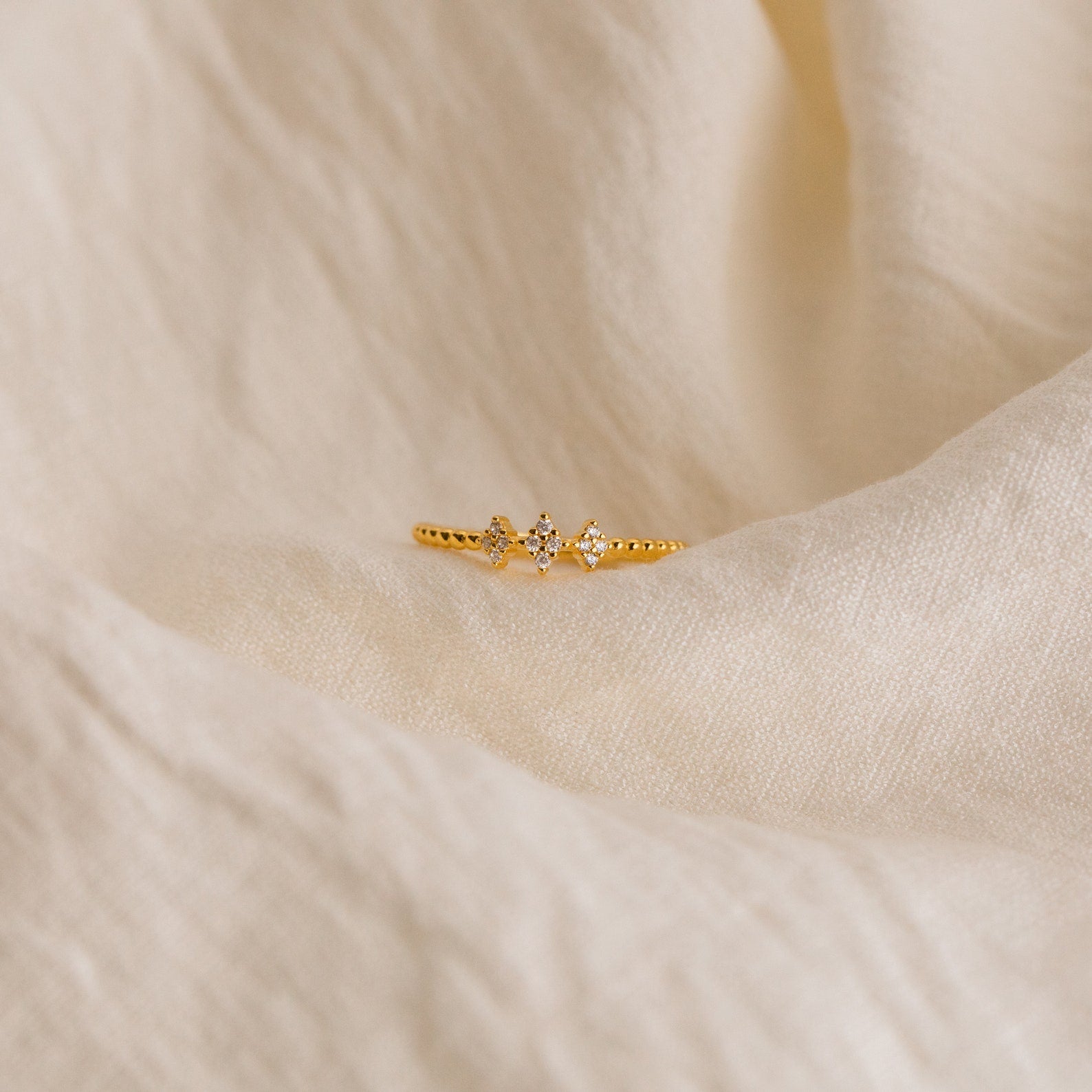 The Jasmine Beaded Diamond Ring, featuring three small diamonds, is displayed on soft cream fabric—ideal for bringing a timeless touch to your ring stack.