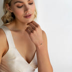 Woman in a cream dress touching her chin, elegantly showcasing the Eloise Gemstone Bracelet and dainty jewelry on her wrist.