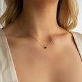 A woman wearing the Onyx Dainty Diamond Necklace—a delicate silver chain with a small black stone pendant—adds timeless elegance to her look.