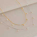 Gold and silver chain necklaces, each adorned with evenly spaced small white pearl drops, displayed on a light surface.