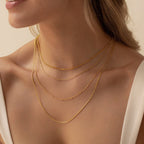 A woman wears layered essential gold chains in different lengths and styles across her neck and collarbone.

