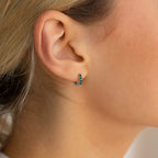 Close-up of a woman’s ear wearing Elise Emerald Huggies, elegant earrings adorned with green gemstones—perfect for lovers of sophisticated green jewelry.