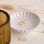 Aria Diamond Drop Studs displayed in a scalloped white dish with lightweight earrings and decor in the background, alongside another pair of sparkling crystal earrings nearby.