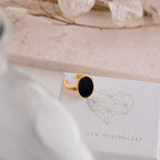 Midnight Hour Onyx Ring with adjustable band, featuring a black oval stone, displayed on a textured box with a geometric heart design.