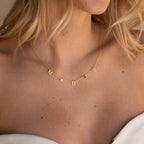A woman wears the Alice Letter Birthstone Necklace with gold M, B, S charms and small gems, paired with a white top—an elegant, personalized jewelry piece and a thoughtful gift idea for mom.