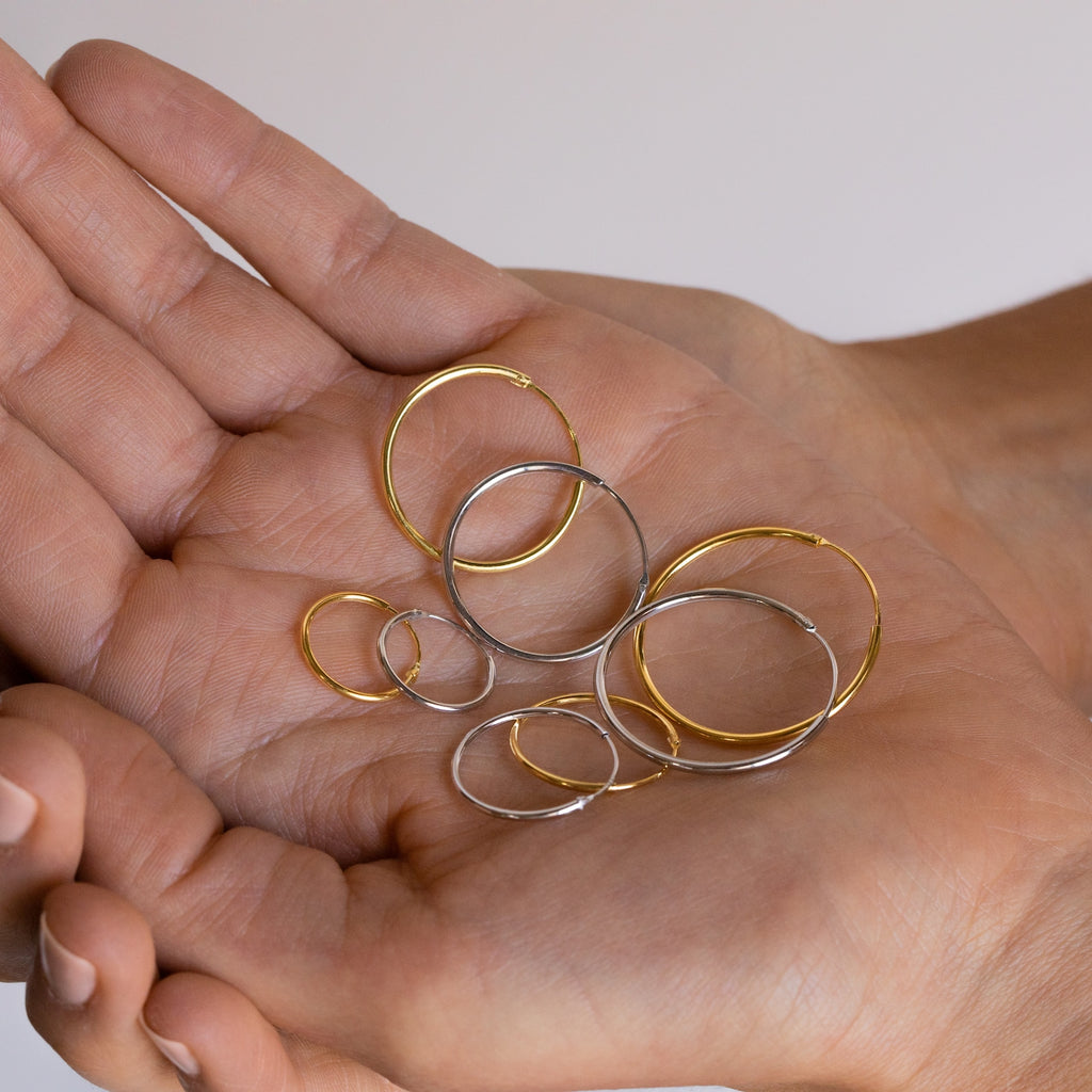 A hand holds several gold and silver Thin Hoops Set earrings in various sizes—classic accessories ideal for everyday wear.