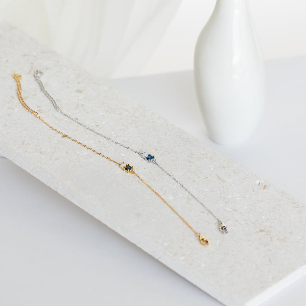 The Eloise Gemstone Bracelet features gold and silver chains with small gemstone charms, ideal for dainty jewelry lovers, displayed on a textured white stone surface.