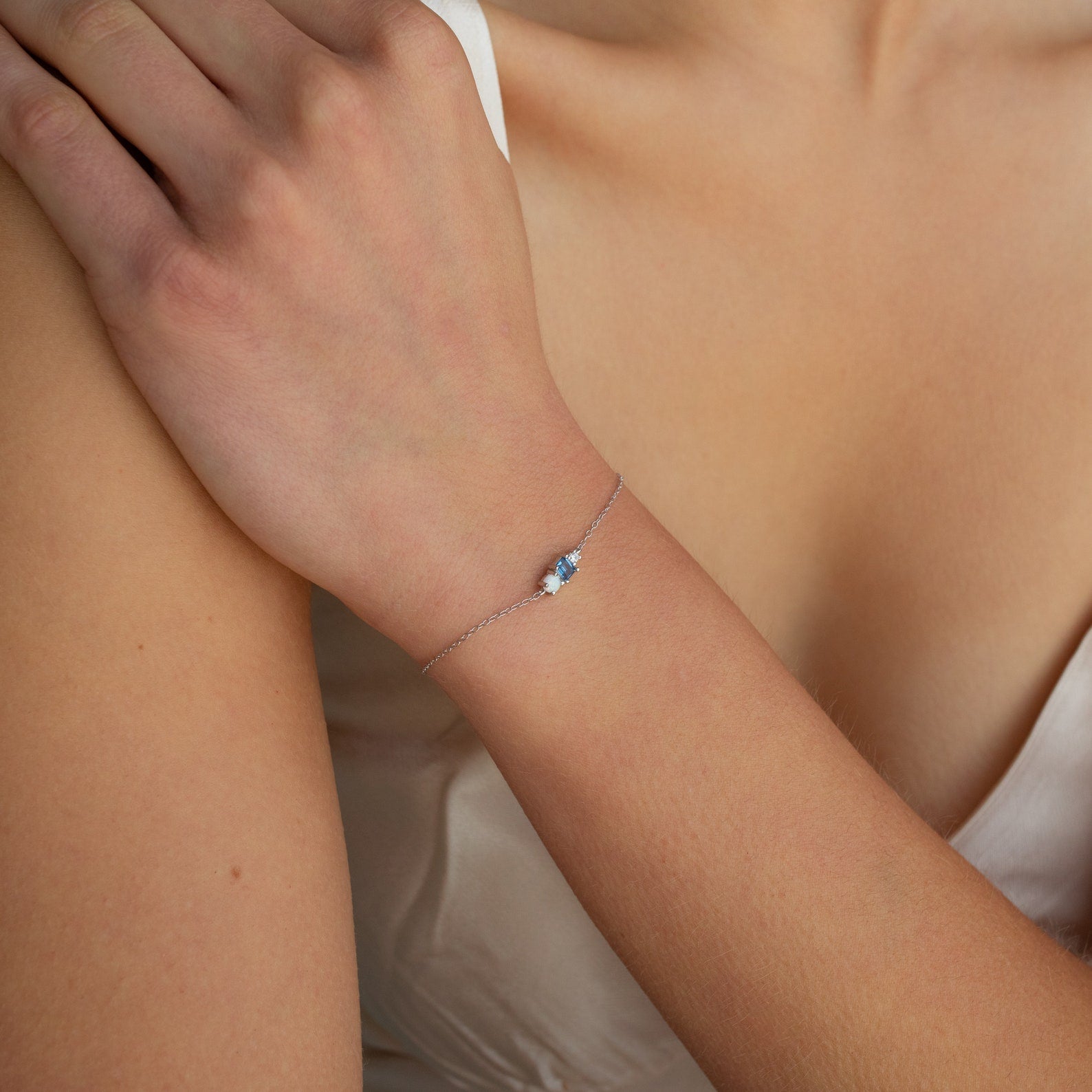 The Eloise Gemstone Bracelet, featuring a delicate silver chain and a blue gemstone flower, graces a woman’s wrist in this close-up, highlighting the beauty of dainty jewelry.