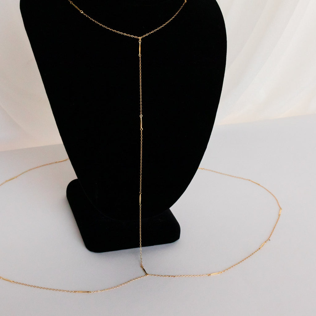 The Kara Body Chain, shown on a black velvet stand with white draped fabric, is the perfect trendy jewelry piece to elevate your summer style.