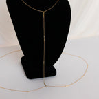 The Kara Body Chain, shown on a black velvet stand with white draped fabric, is the perfect trendy jewelry piece to elevate your summer style.