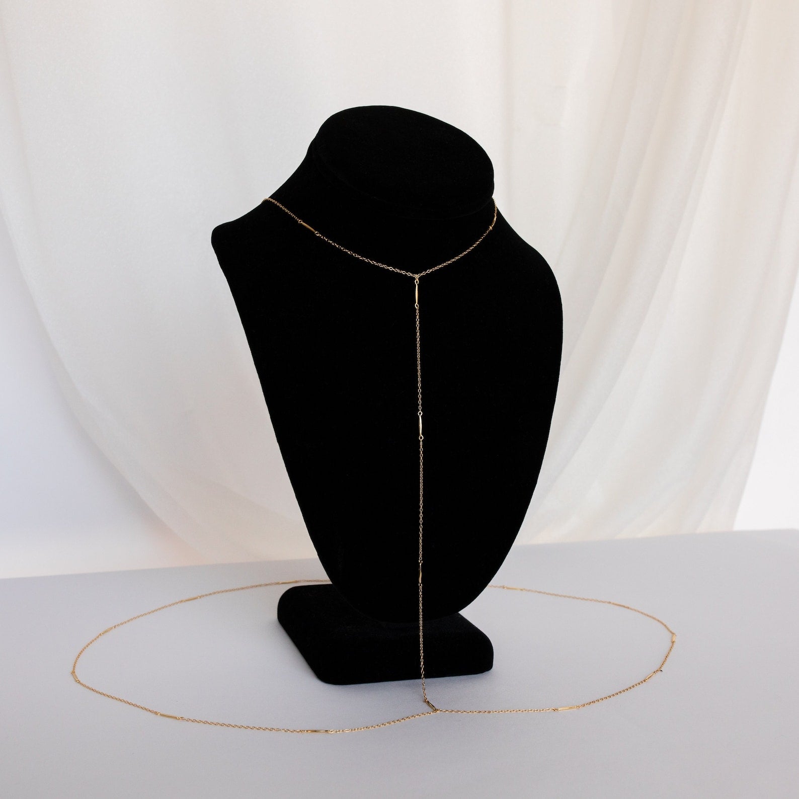 The Kara Body Chain is displayed on a black velvet bust with a white fabric background—an on-trend accessory to enhance your summer jewelry collection.