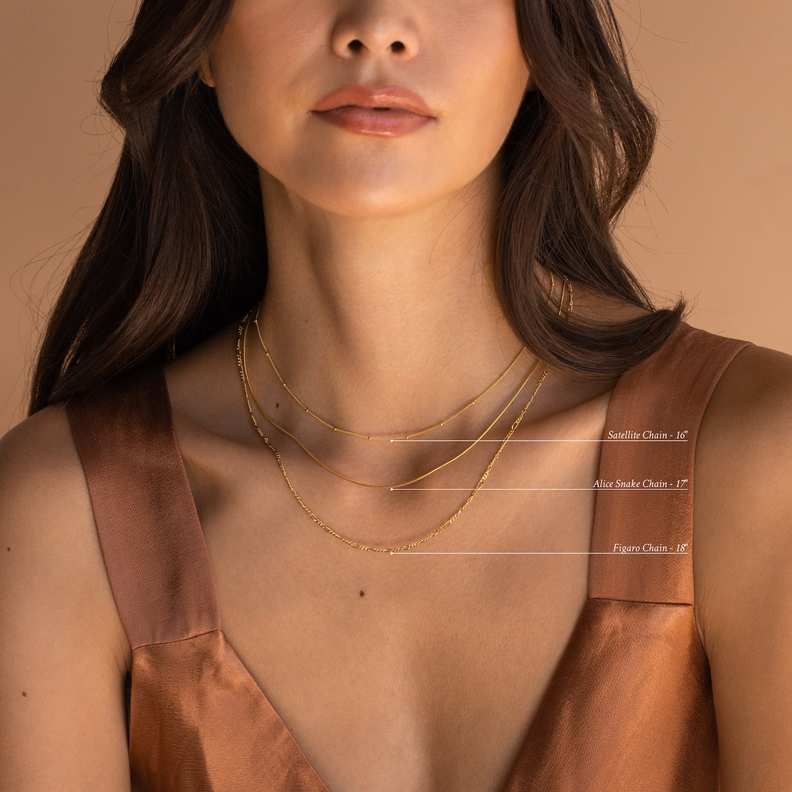 A woman wears three labeled gold chains: Satellite Chain (16”), Alice Snake Chain (17”), and Figaro Chain (18”).