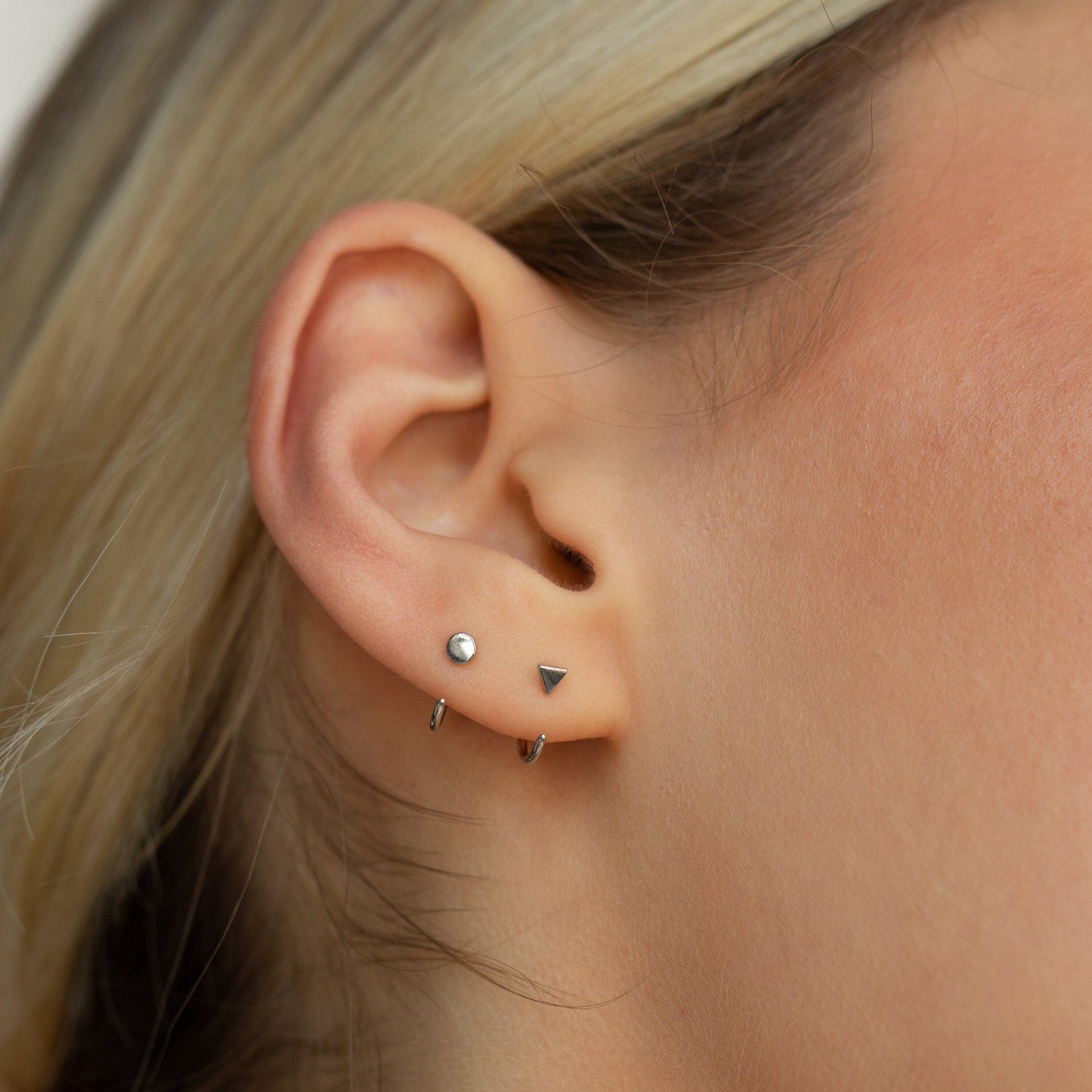 Close-up of an ear wearing the Tiny Circle & Triangle Huggies—lightweight, stylish earrings featuring a small hoop, silver stud, and triangle design, perfect for everyday wear.