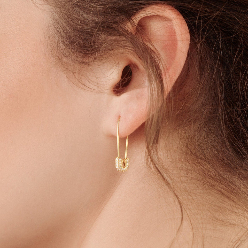 A close-up of a woman’s ear wearing a small textured gold hoop paired with our Pave Safety Pin Earrings, creating an edgy yet elegant look.