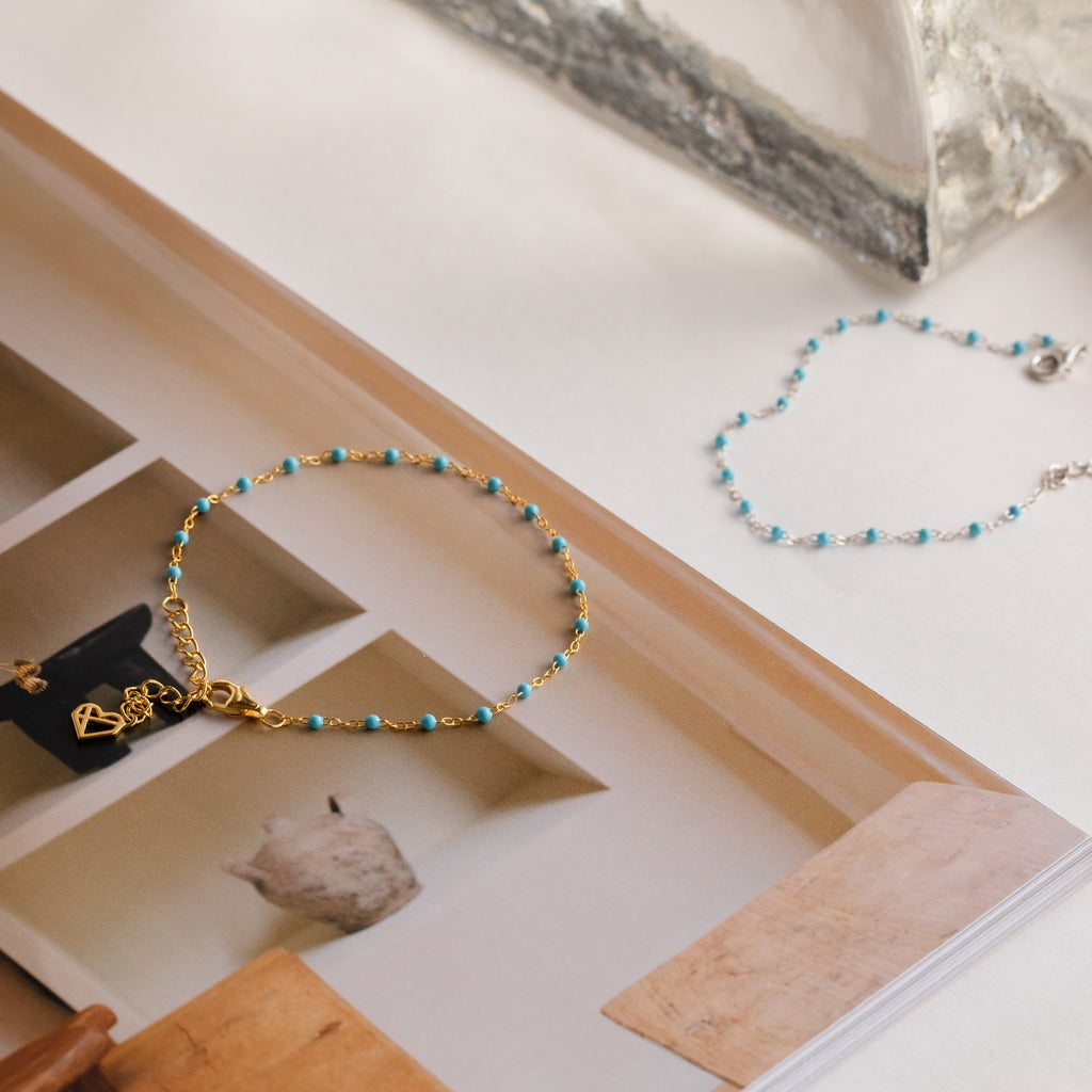 A Turquoise Station Bracelet sits on an open magazine, complemented by a silver and turquoise boho bracelet—perfect for creating a chic bracelet stack.