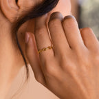 A hand wearing the Reese Link Ring, a minimalist chain design, gently touches the side of a person’s face near their ear.
