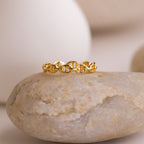 The Reese Link Ring, a minimalist gold chain design, is displayed atop a smooth beige stone against a neutral background.