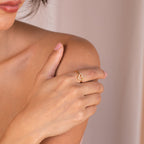 Woman wearing the Aphrodite Pave Heart Ring, its diamond accents sparkling as she gently touches her shoulder against a soft, neutral background.