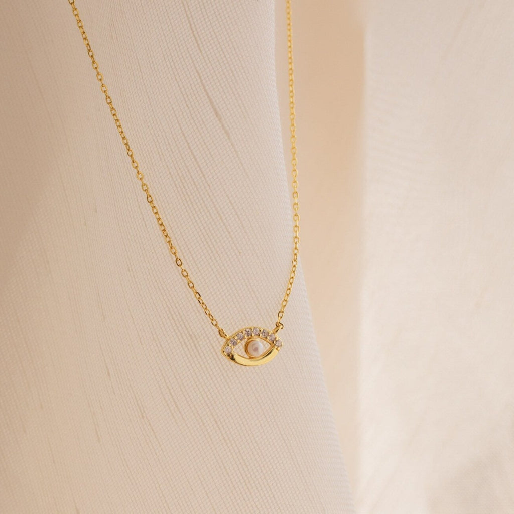 Amaryllis Pave Evil Eye Necklace in 18K Gold featuring a sparkling pendant, shown against a soft cream-colored fabric background.
