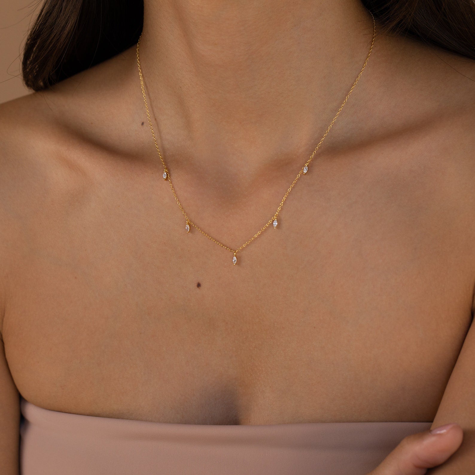 A woman in a strapless nude top wears the Marquise Station Necklace, featuring marquise-shaped diamonds and teardrop charms on a delicate chain.