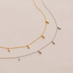 The Marquise Station Necklace, in both gold and silver, features a dainty chain adorned with small marquise-shaped diamond charms and is elegantly displayed on a light background.