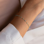 The Turquoise Station Bracelet, a delicate gold chain with small turquoise beads, is styled as a boho bracelet and pairs perfectly with a white long-sleeve shirt.