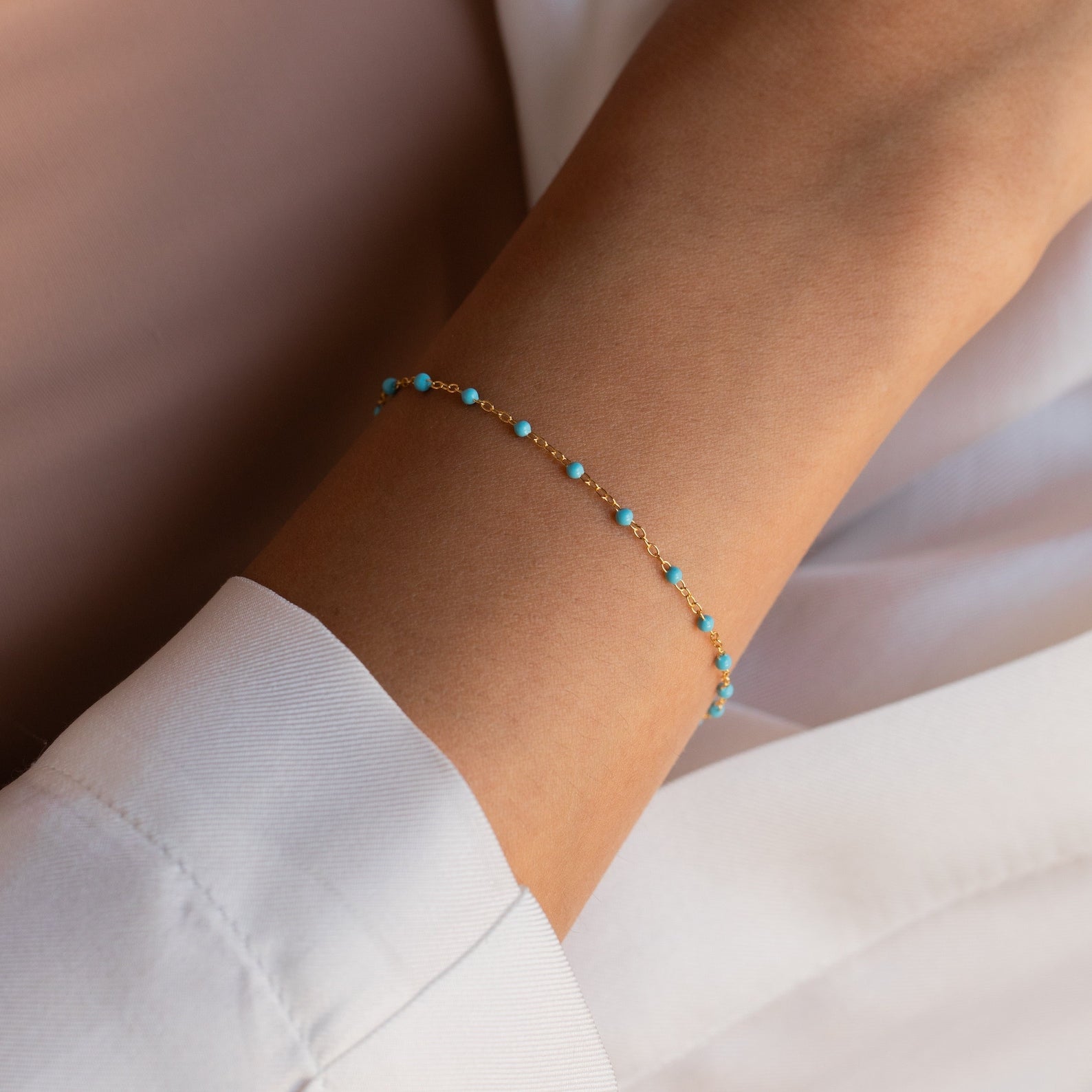 The Turquoise Station Bracelet, a delicate gold chain with small turquoise beads, is styled as a boho bracelet and pairs perfectly with a white long-sleeve shirt.
