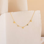 The Alice Letter Birthstone Necklace features gold W, B, S charms and two sparkling gemstones on a white textured background—a unique personalized piece and thoughtful gift for mom.