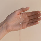 A hand holds a delicate gold Sideways Initial Birthstone Necklace with a pendant shaped like the letter E—an elegant Gift for Mom.