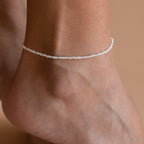 A foot wearing the Brinley Pearl Anklet, which is composed of dainty freshwater pearls strung together, shimmering in the light.