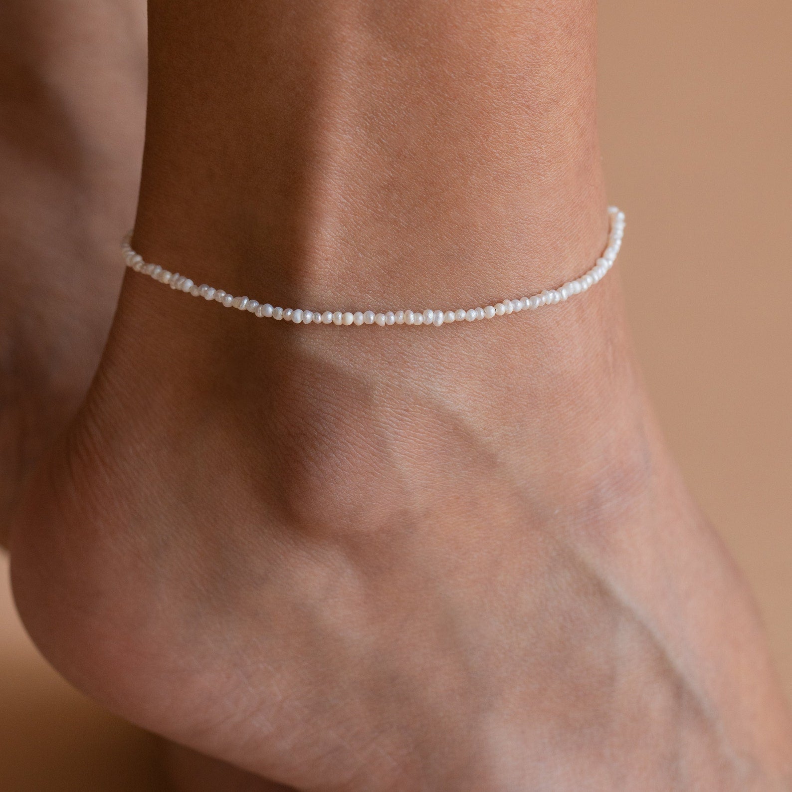 A foot wearing the Brinley Pearl Anklet, which is composed of dainty freshwater pearls strung together, shimmering in the light.