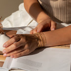A woman’s hand, adorned with Essential Bracelet Chains, rests on an open magazine in soft natural light.