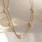 The Anna Pearl Station Necklace features two-tone layers with pearls on silver and gold chains, displayed on a softly lit surface—an elegant pick for Mother's Day or as a timeless bridesmaids gift.