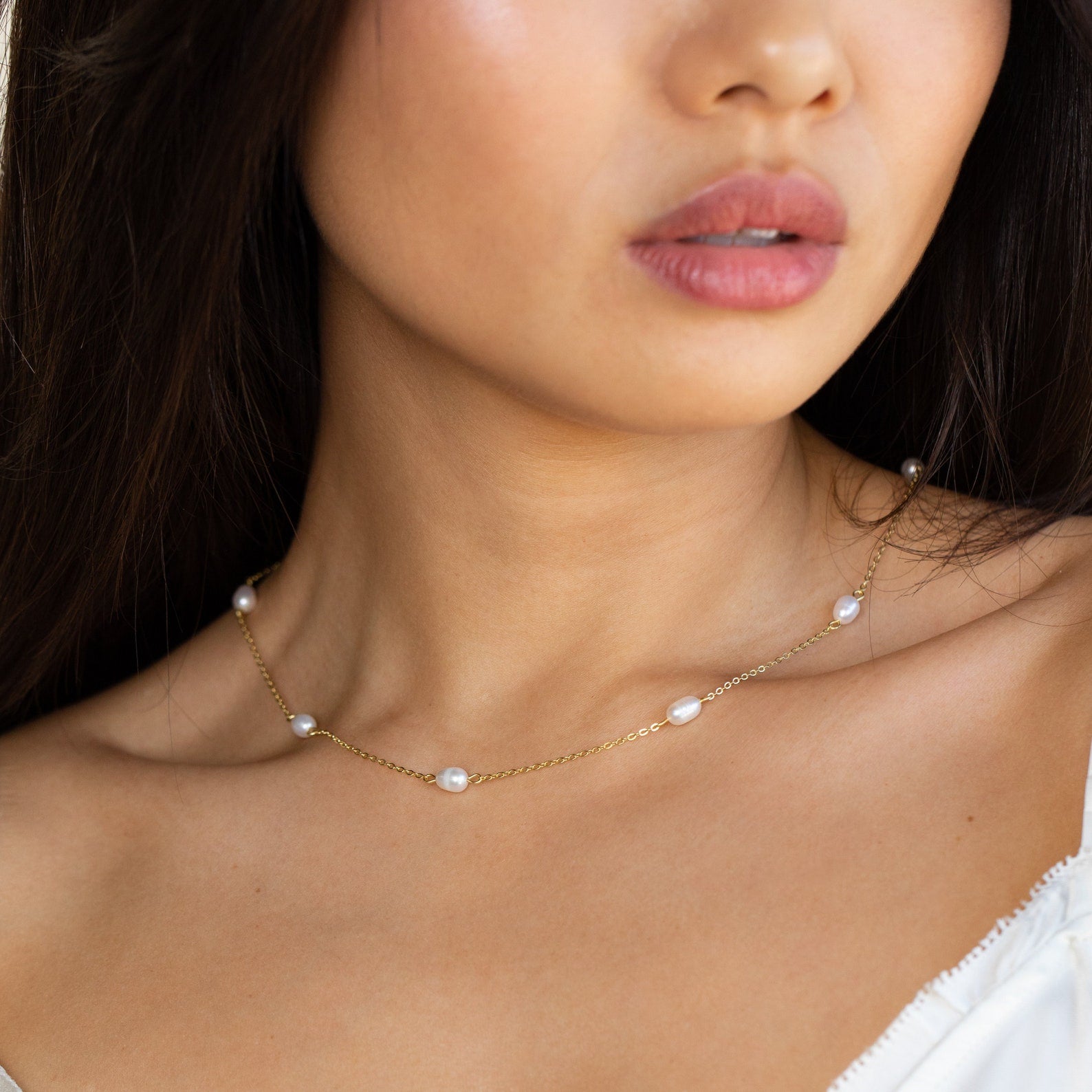 A woman wears the Anna Pearl Station Necklace, a delicate gold piece with evenly spaced small pearls—perfect as a bridesmaid gift or for Mother’s Day.