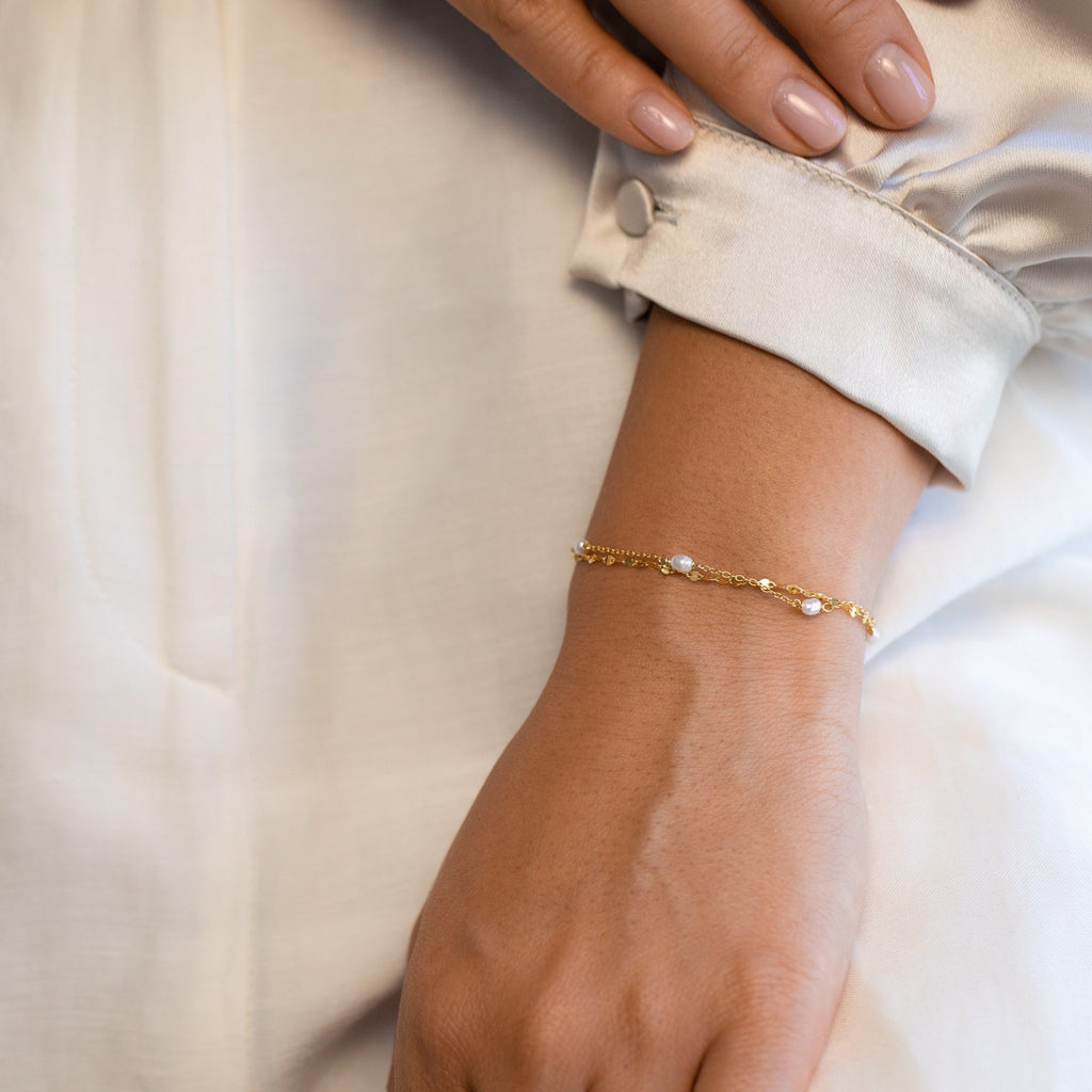 Hand resting gently on neutral-toned fabric while wearing the Magnolia Pearl Wrap Bracelet, styled as an everyday elegant accessory.